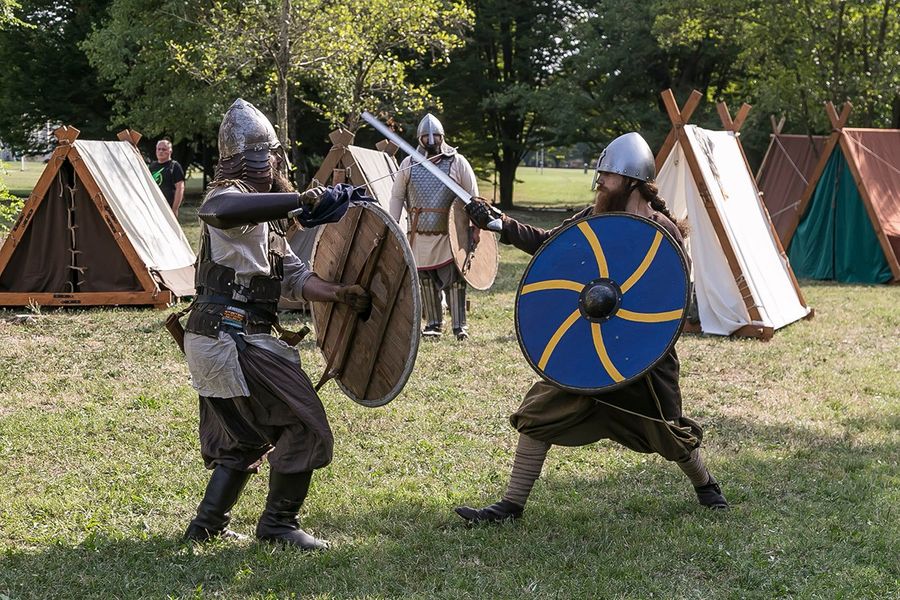 Due uomini vestiti in abiti da guerrieri medievali inscenano un combattimento con spade e scudi