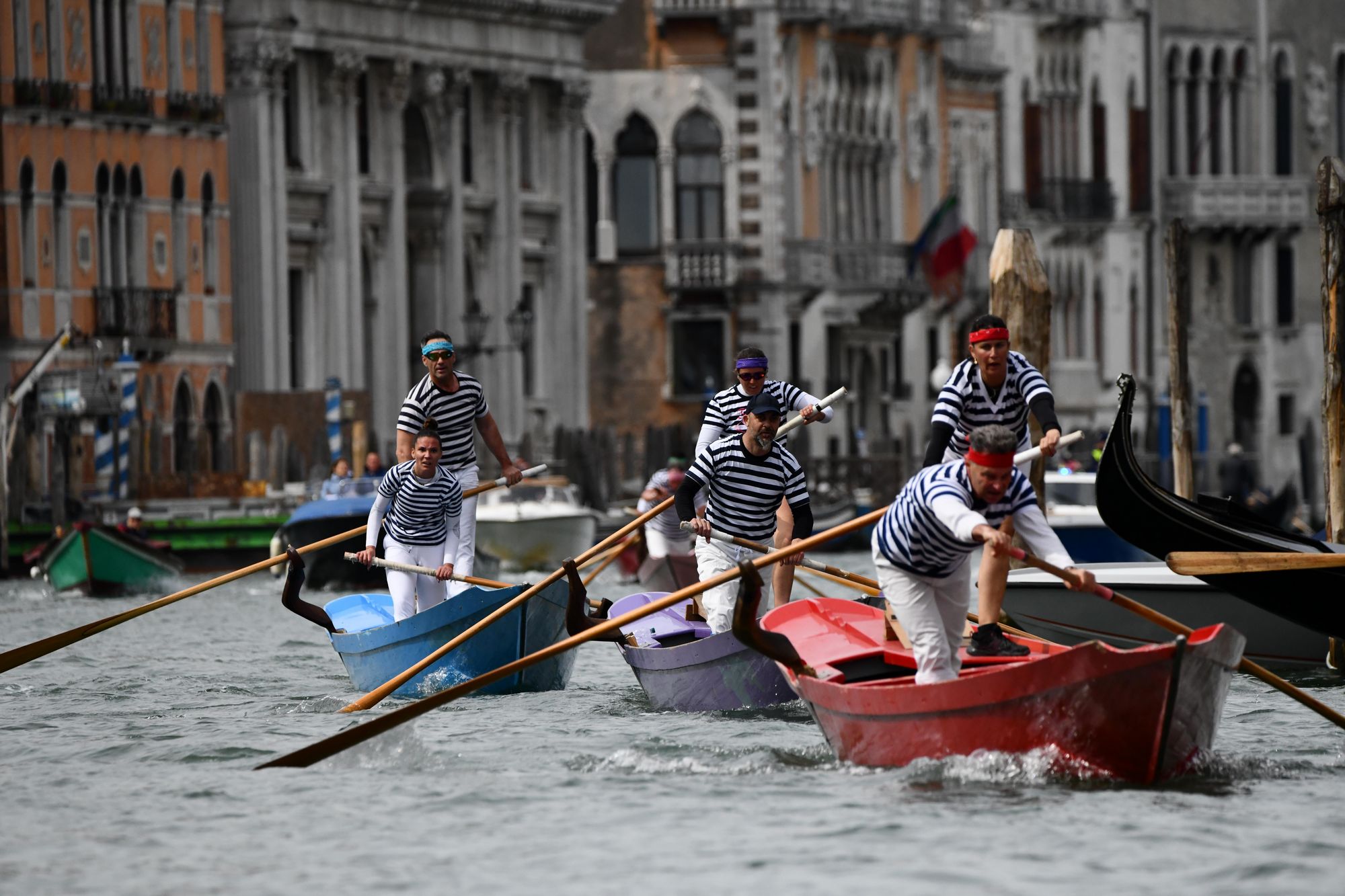 Tre equipaggi di due rematori con maglia a righe orizzontali vogano su pupparini veneziani in Canal Grande