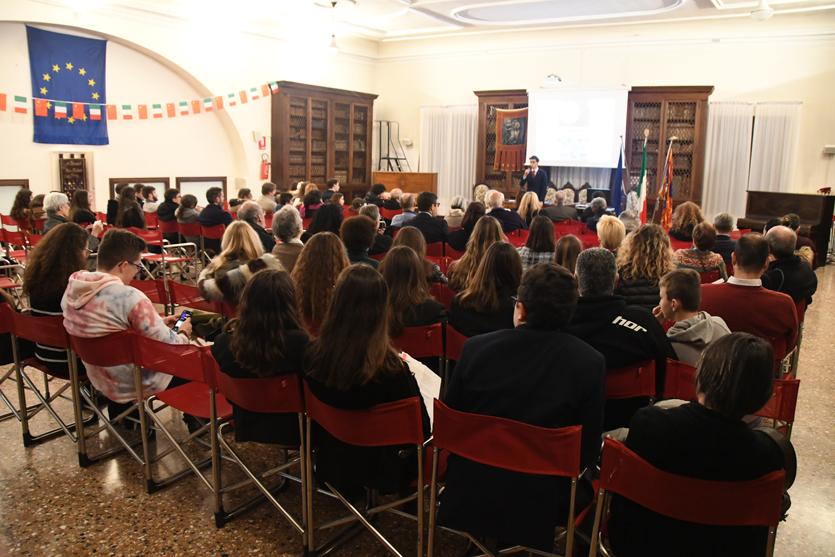 Platea di adulti e studenti visti di spalle, a una conferenza