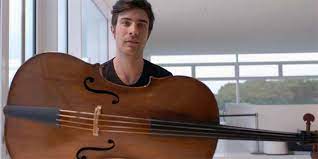 Violoncello in orizzontale e, dietro, uomo di cui si vedono solo testa e spalle