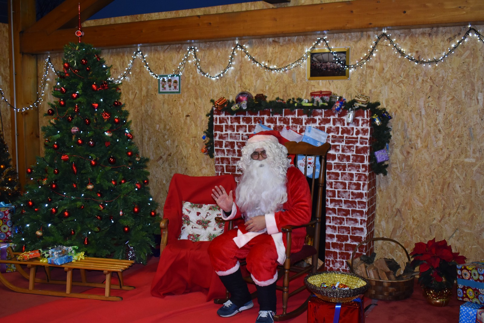 Babbo Natale in posa davanti a un camino e di fianco a un albero di Natale