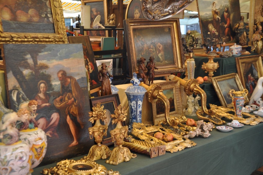 Quadri, candelabri e vasi d'antiquariato esposti sul banchetto di un mercatino