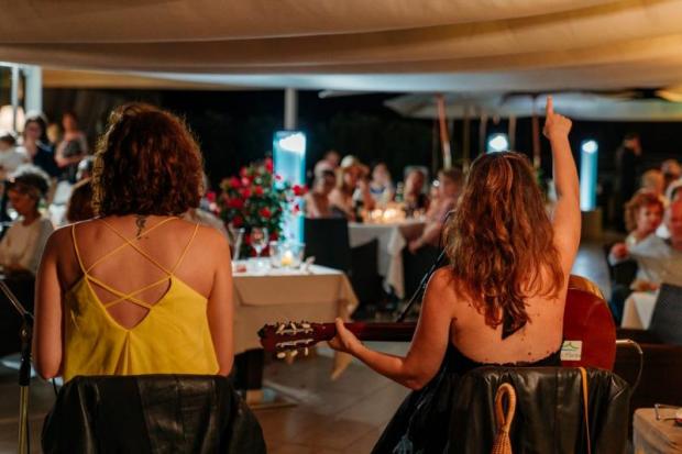 Due donne sedute viste di spalle, quella di dx col braccio dx alzato