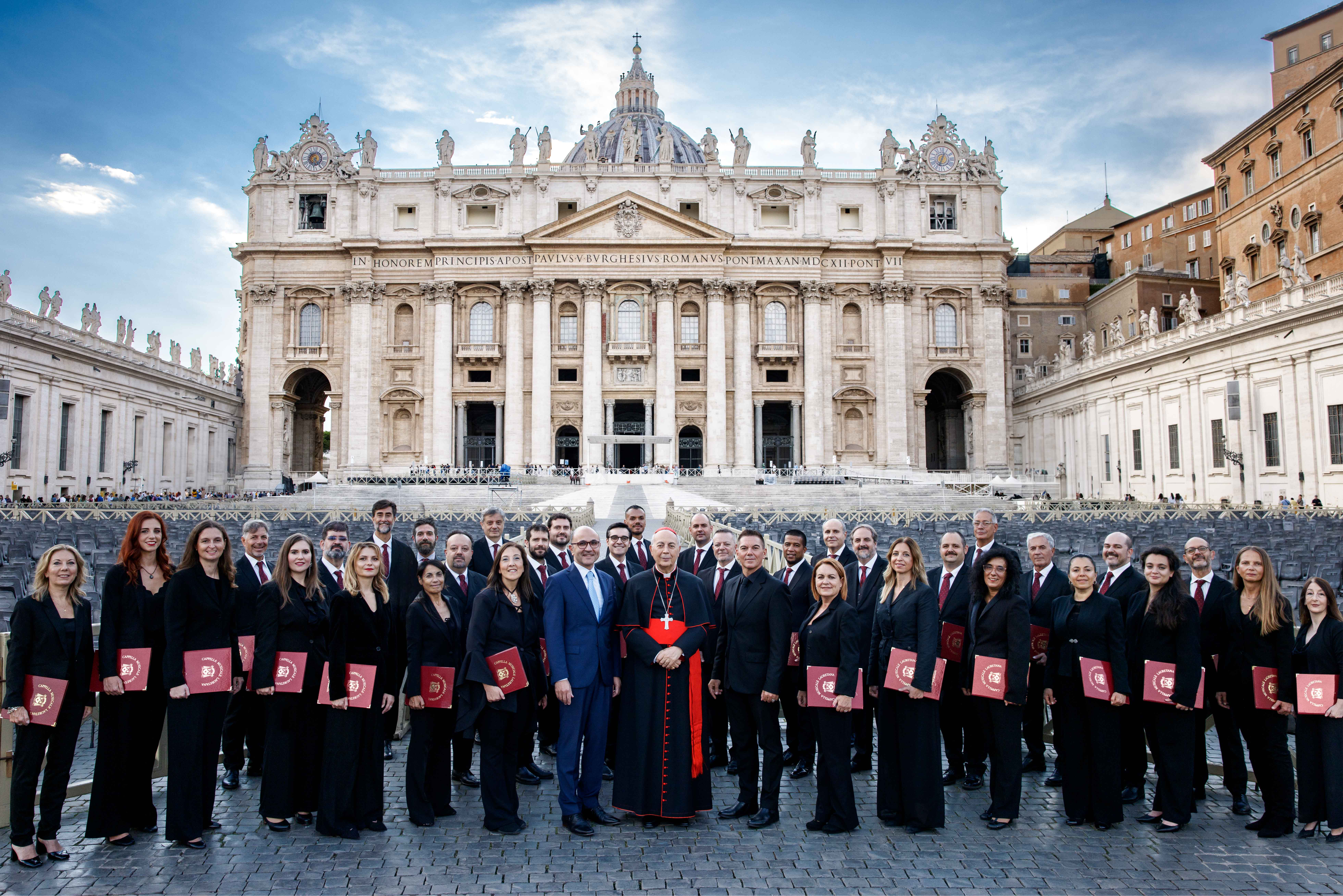 Folto gruppo di persone, con al centro in cardinale, schierato davanti alla Basilica di San Pietro a Roma