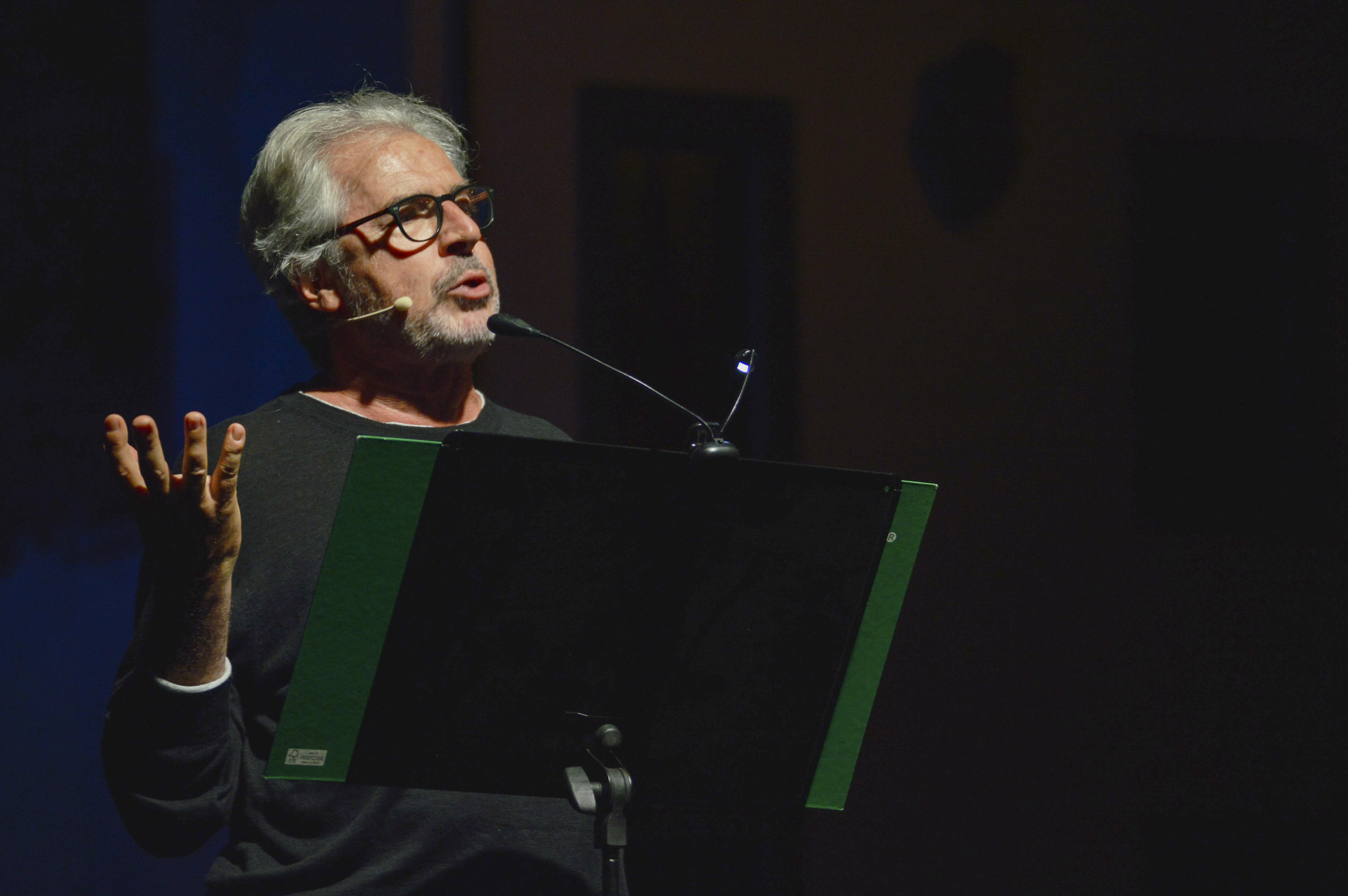 Primo piano di Tullio Solenghi che recita di fronte a un leggio