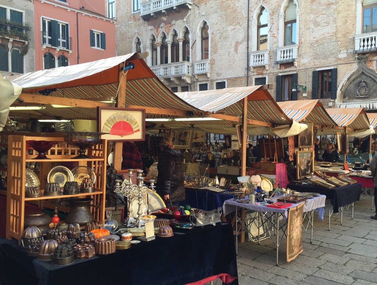 Cinque banchetti carichi di oggetti di antiquariato in un campo veneziano